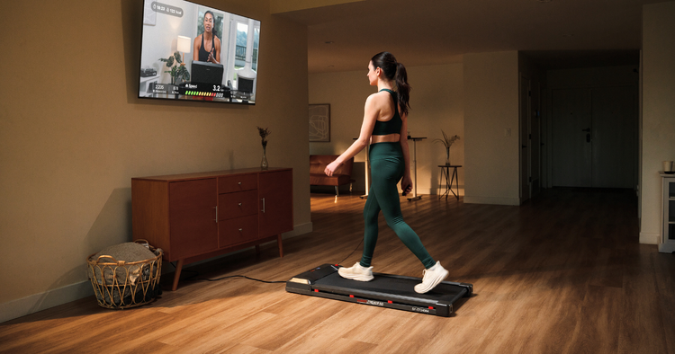 woman walks on treadpad in her home and follows along to workout on her TV