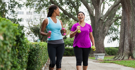two women walk outdoors together holding small weights for low impact and low intensity workout