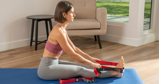woman uses yoga stretch strap to stretch on blue yoga mat in her home