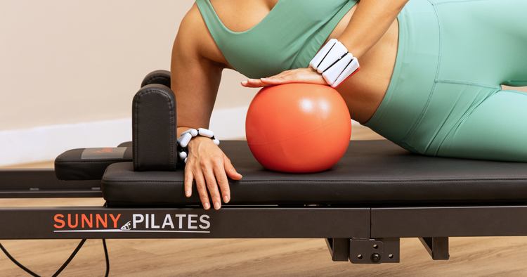 women on reformer Pilates with a Pilates ball and wrist weights