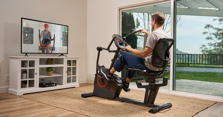 man follows along to a recumbent elliptical workout in his home