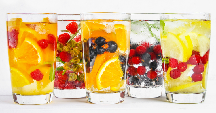 5 glasses of water with fruits like oranges, lemon, and berries.