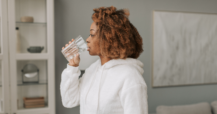 woman drinks glass of water in home with sweatshirt on