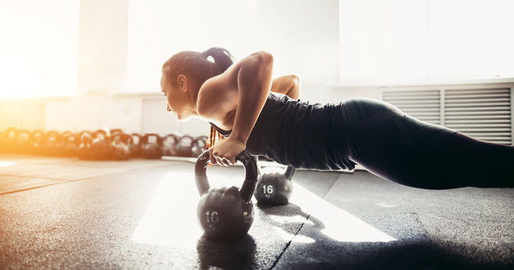 a woman is pushing up with kettlebells