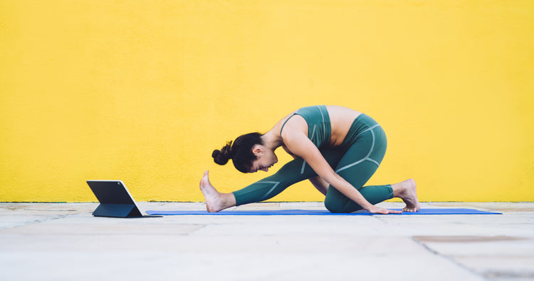 a woman is doing half split posture on yoga mat with tablet near on yellow background