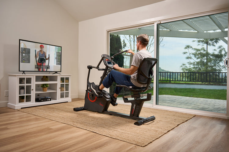 Man using Sunny Health & Fitness recumbent bike at home with SunnyFit app on TV – HSA/FSA eligible exercise equipment